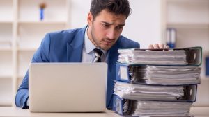 Man staring at a huge pile of documents in binders